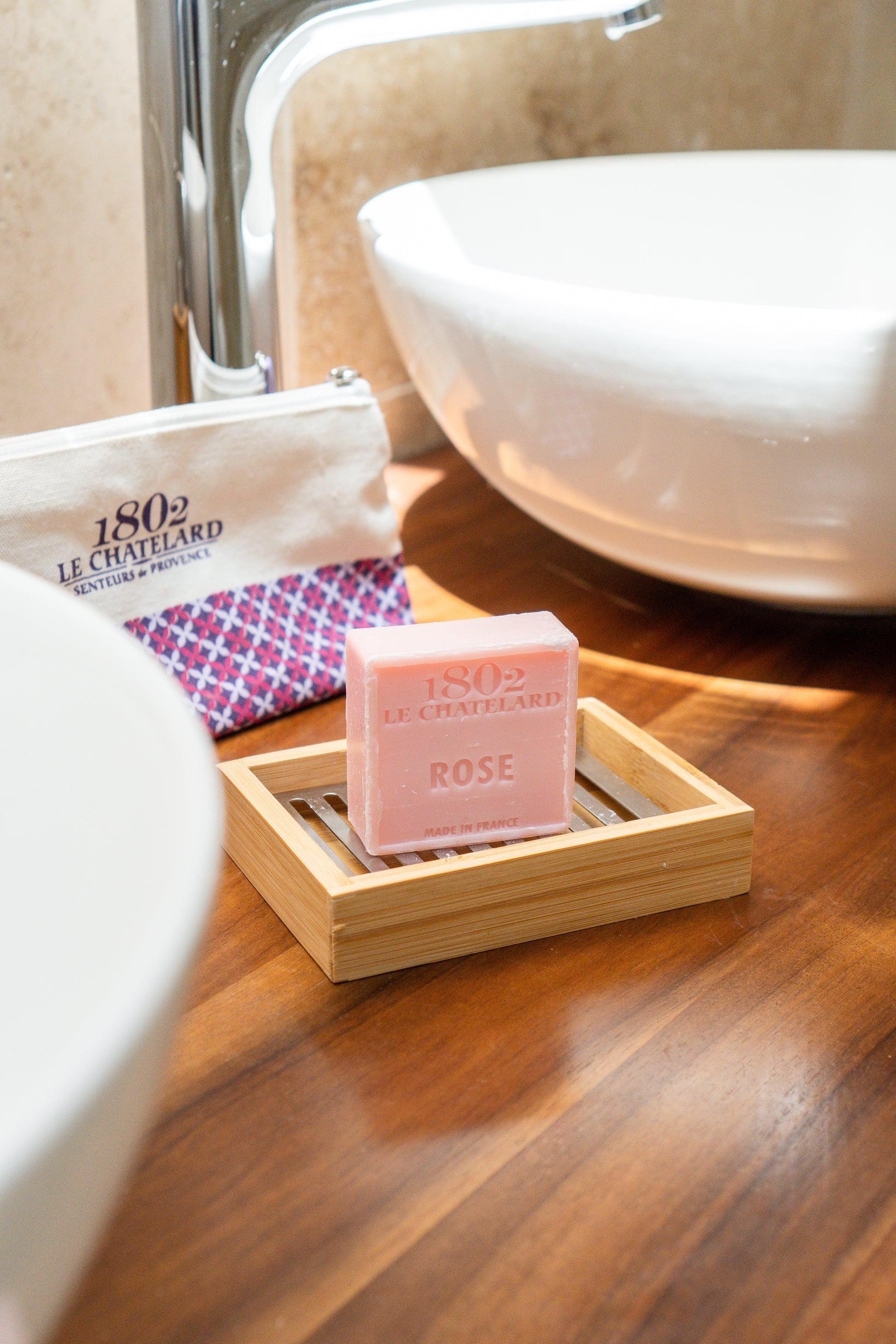 Pink soap bar on a wooden soap dish with a white sink in the background