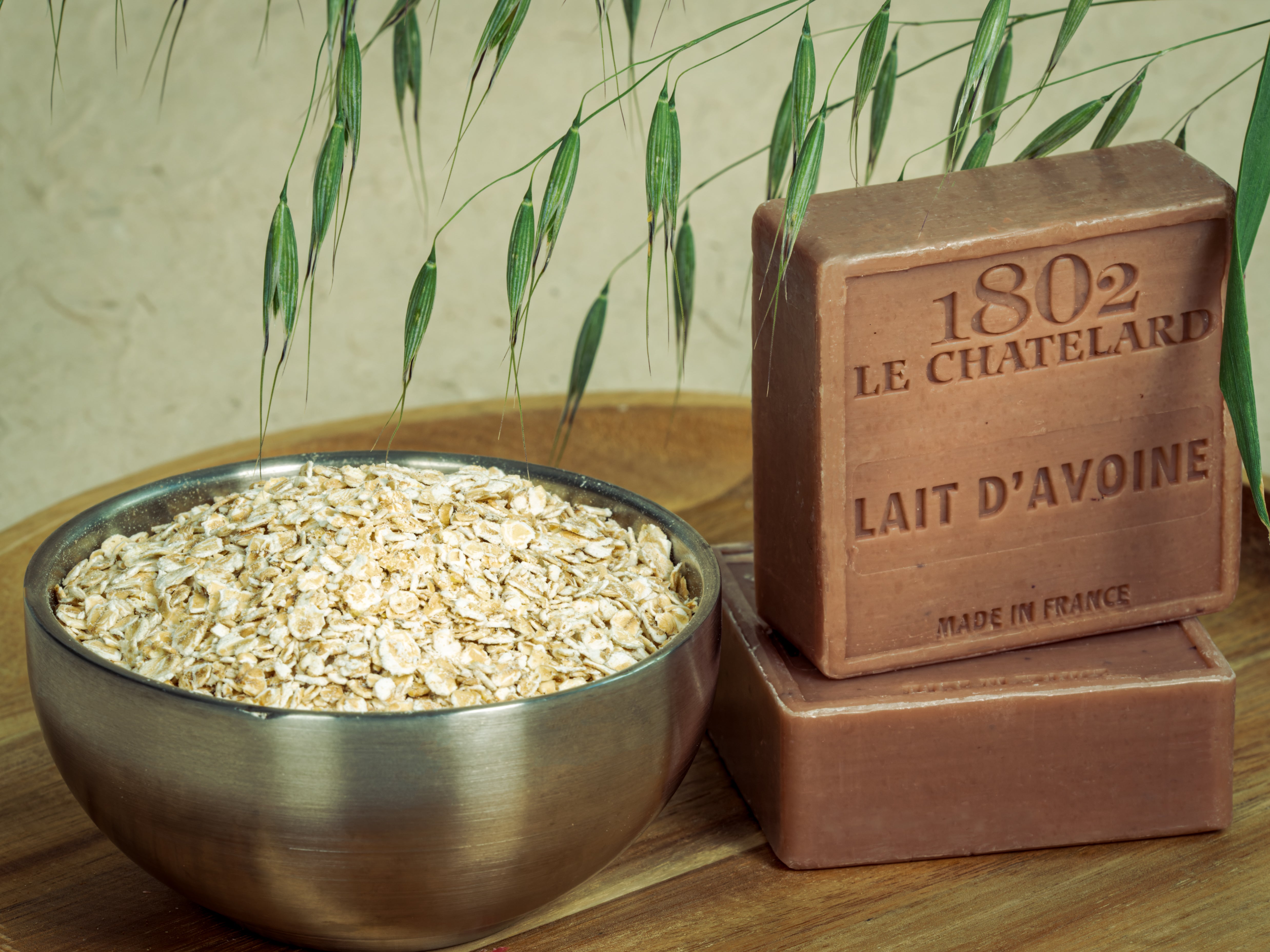 Two bars of soap labeled '1802 Le Chatelard' next to a bowl of oats on a wooden surface with a natural background.
